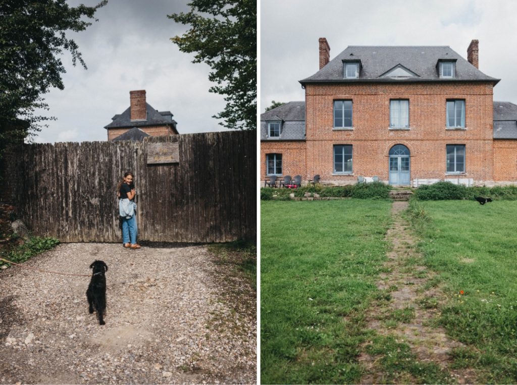 Links: Eine Frau mit einem schwarzen Hund an der Leine steht vor einem hohen Holztor, aufgenommen von Fotograf Köln. Rechts: Ein großes Backsteinhaus mit blauen Türen und Fenstern steht am Ende eines grasbewachsenen Hofes mit einem Steinweg und einem wolkenverhangenen Himmel darüber.