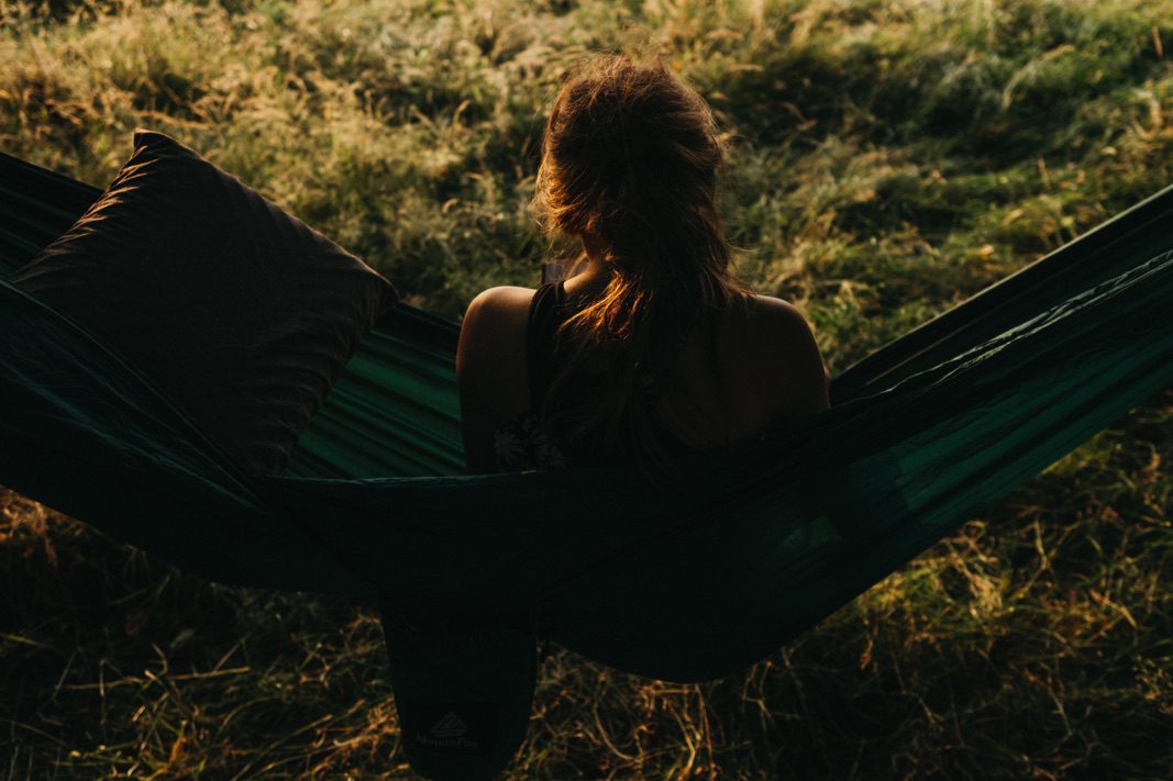 Eine Person mit langen Haaren sitzt in einer grünen Hängematte im Freien, das Sonnenlicht beleuchtet ihre Haare und das Gras. Neben ihr liegt ein dunkles Kissen, das eine friedliche Szene schafft - die perfekte Inspiration für jeden Familienfotograf oder Fotografin in Köln.