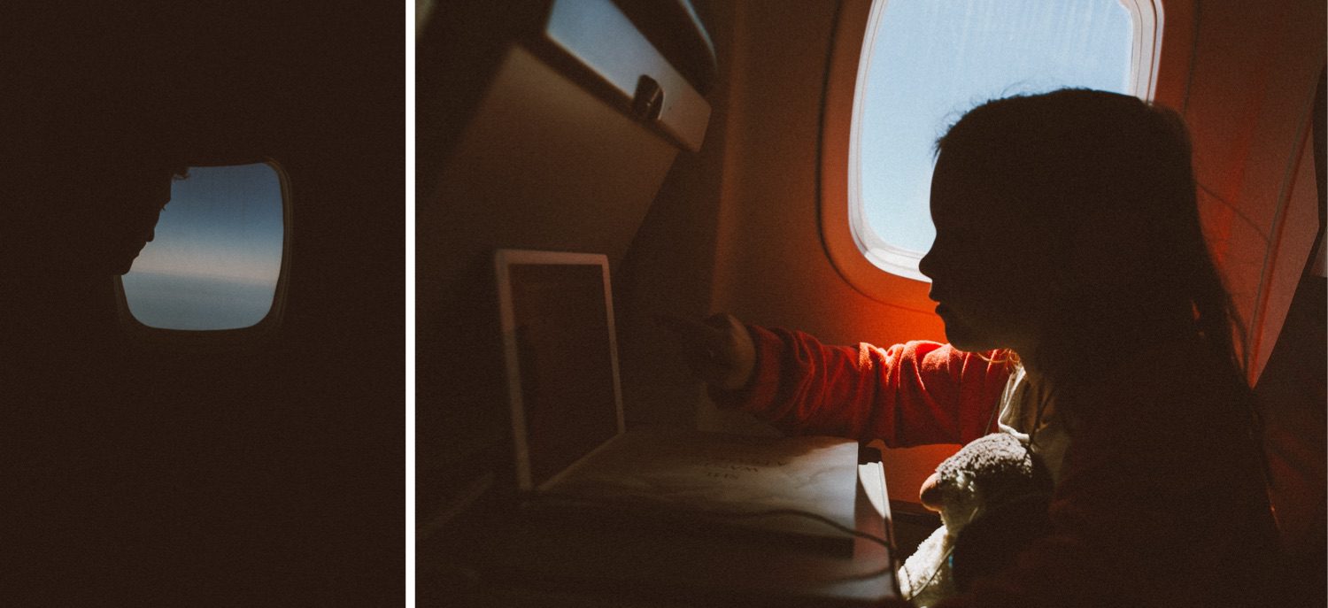 Ein Kind sitzt am Fenster eines Flugzeugs, beleuchtet vom Sonnenlicht, und schaut mit einem Stofftier in der Hand auf ein Tablet. Die Silhouette eines anderen Passagiers, der von einem Familienfotografen aufgenommen wurde, ist durch ein Fenster in einem separaten Panel zu sehen.