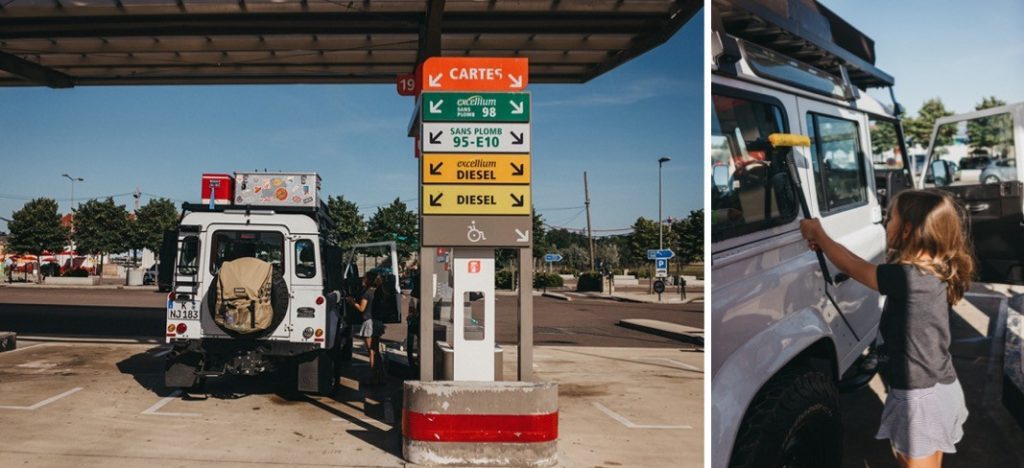 Ein weißer Geländewagen tankt bei klarem Himmel an einer Tankstelle, an deren Tür ein Mädchen steht. Die von einem Familienfotografen aufgenommene Szene wirkt offen und warm, während auf den Tankstellenschildern die Optionen für Benzin und Diesel angezeigt werden.