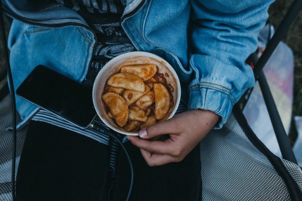 Eine Person in Jeansjacke hält eine Schüssel mit Knödeln oder Pierogi auf dem Schoß, in der Nähe liegt ein schwarzes Smartphone - perfekt eingefangen von einer talentierten Fotografin aus dem Fotostudio Köln.