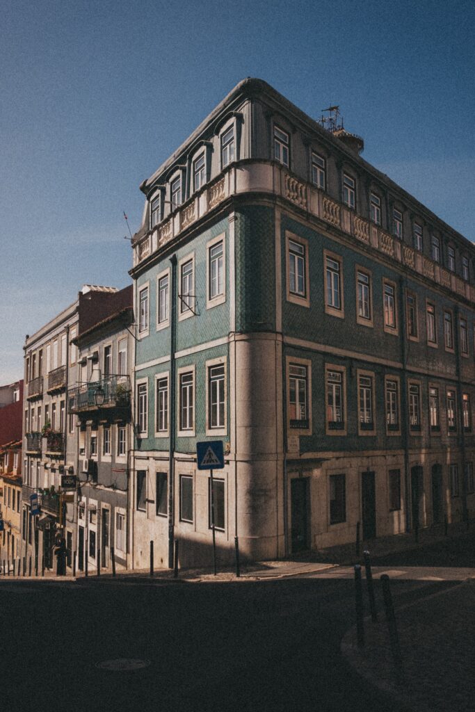 Ein grün-weißes historisches Gebäude mit vielen Fenstern steht an einer schrägen Straßenecke unter einem strahlend blauen Himmel - eine einladende Szene für einen Kinder- oder Familienfotografen, um sie im weichen Sonnenlicht des späten Nachmittags festzuhalten.