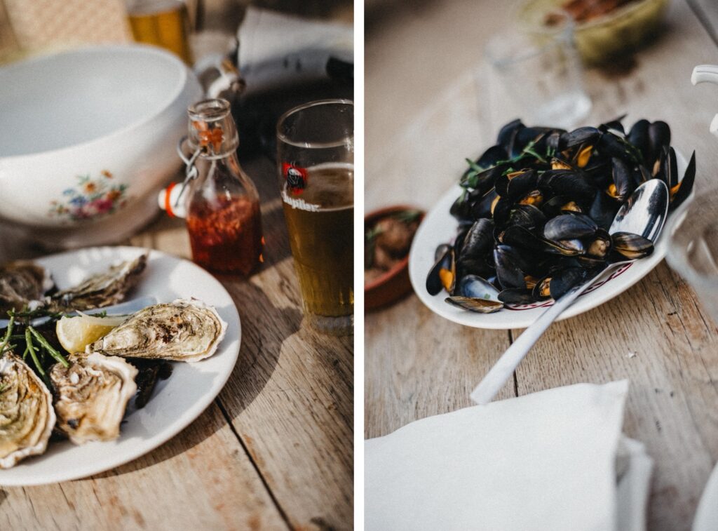 Zwei Teller mit Meeresfrüchten auf einem Holztisch - Austern mit Zitronenspalten und gekochte Muscheln - wurden von einem Werbefotografen kunstvoll arrangiert, der eine rustikale, zwanglose Speiseszene mit Getränken, Soßenflasche und Serviette in der Nähe festhält.